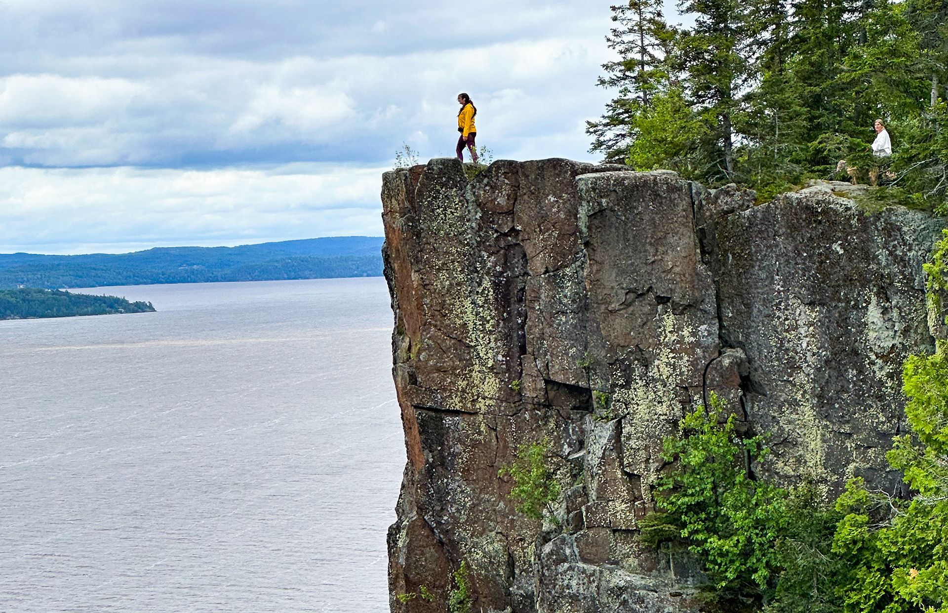 a young woman stands at the edge of a very tall stone cliff