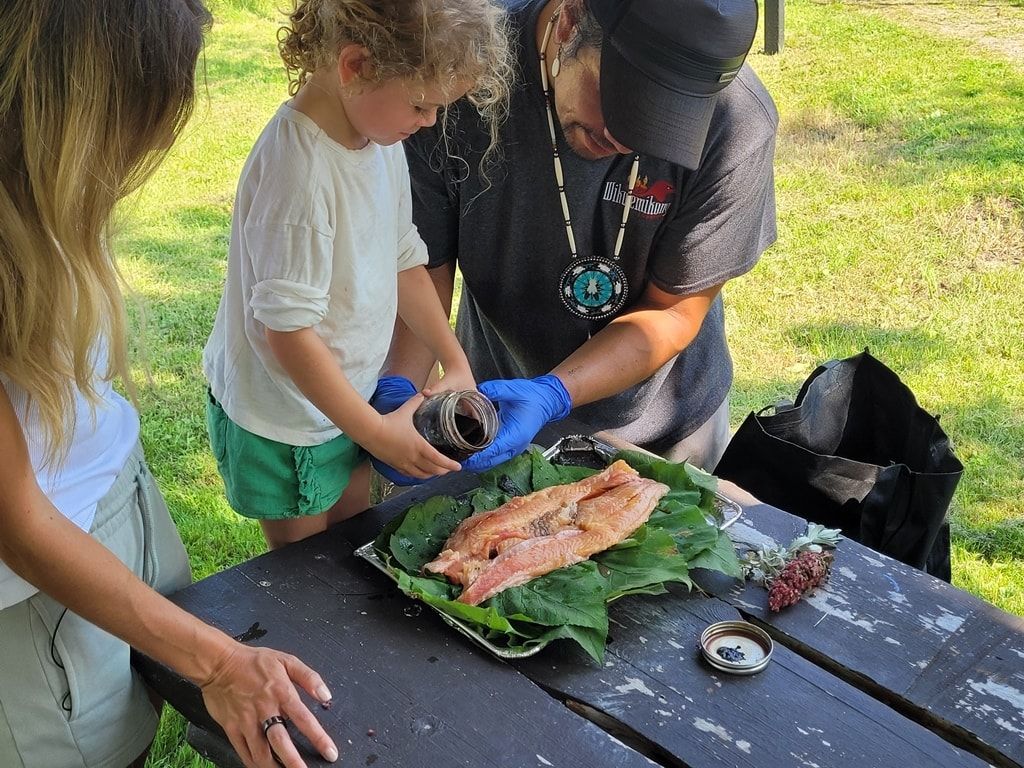 a man helps a young girl pour traditional seasonings over a fillet of fish