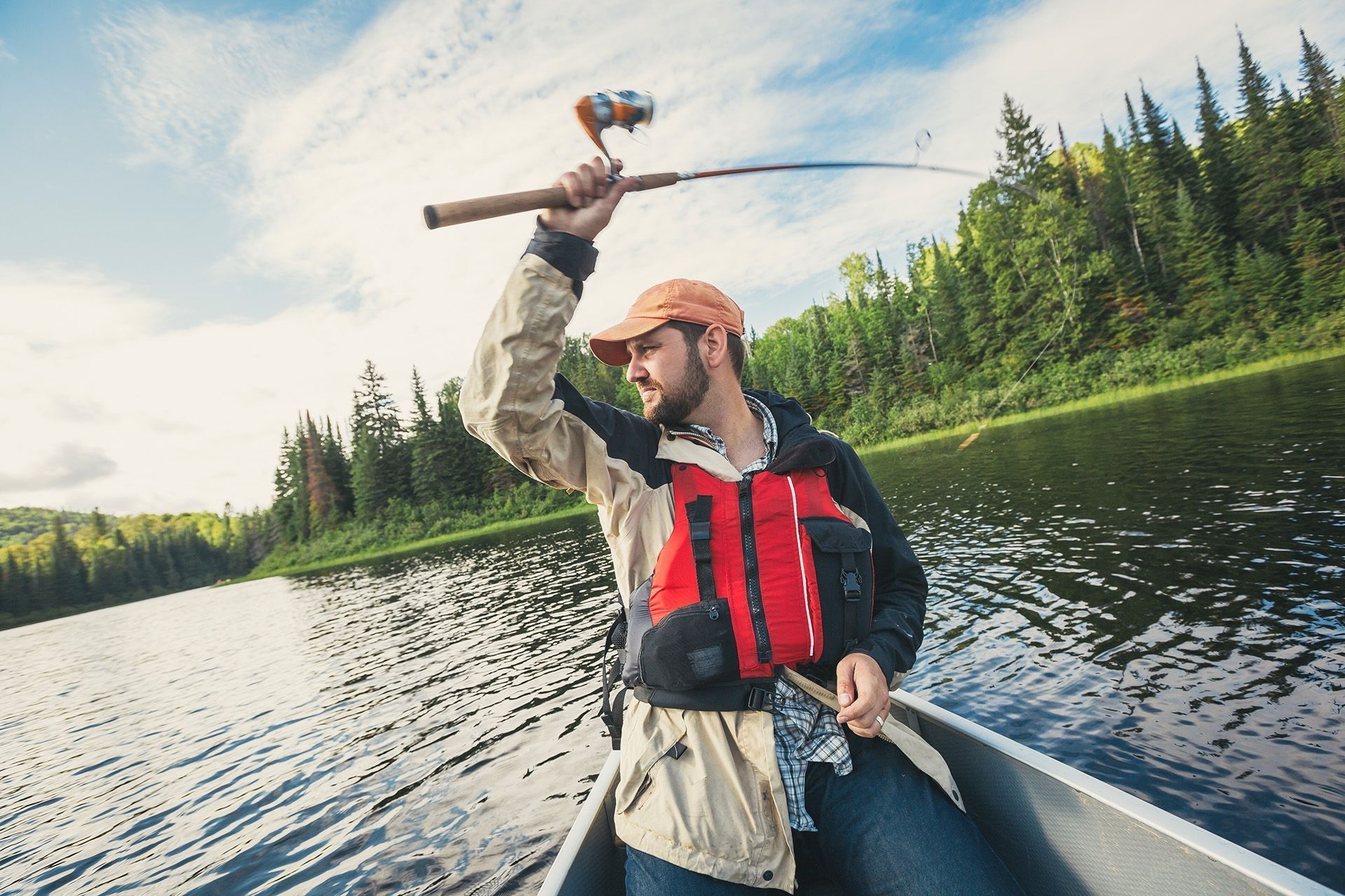 A young man is casting his fishing line by throwing his rod behind his head.