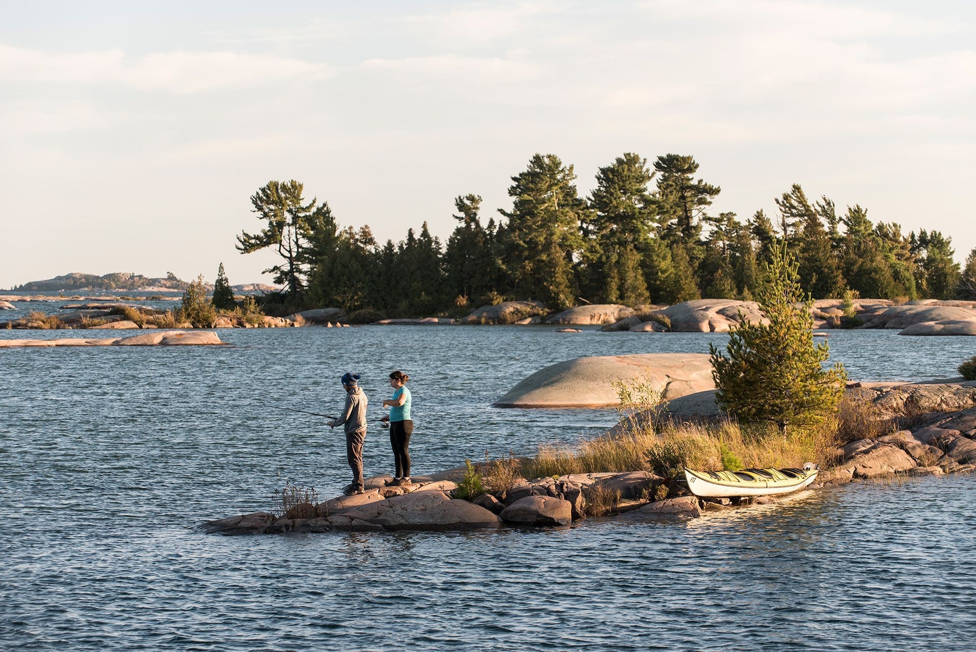 People fishing on a small rocky peninsula in the early morning sun.