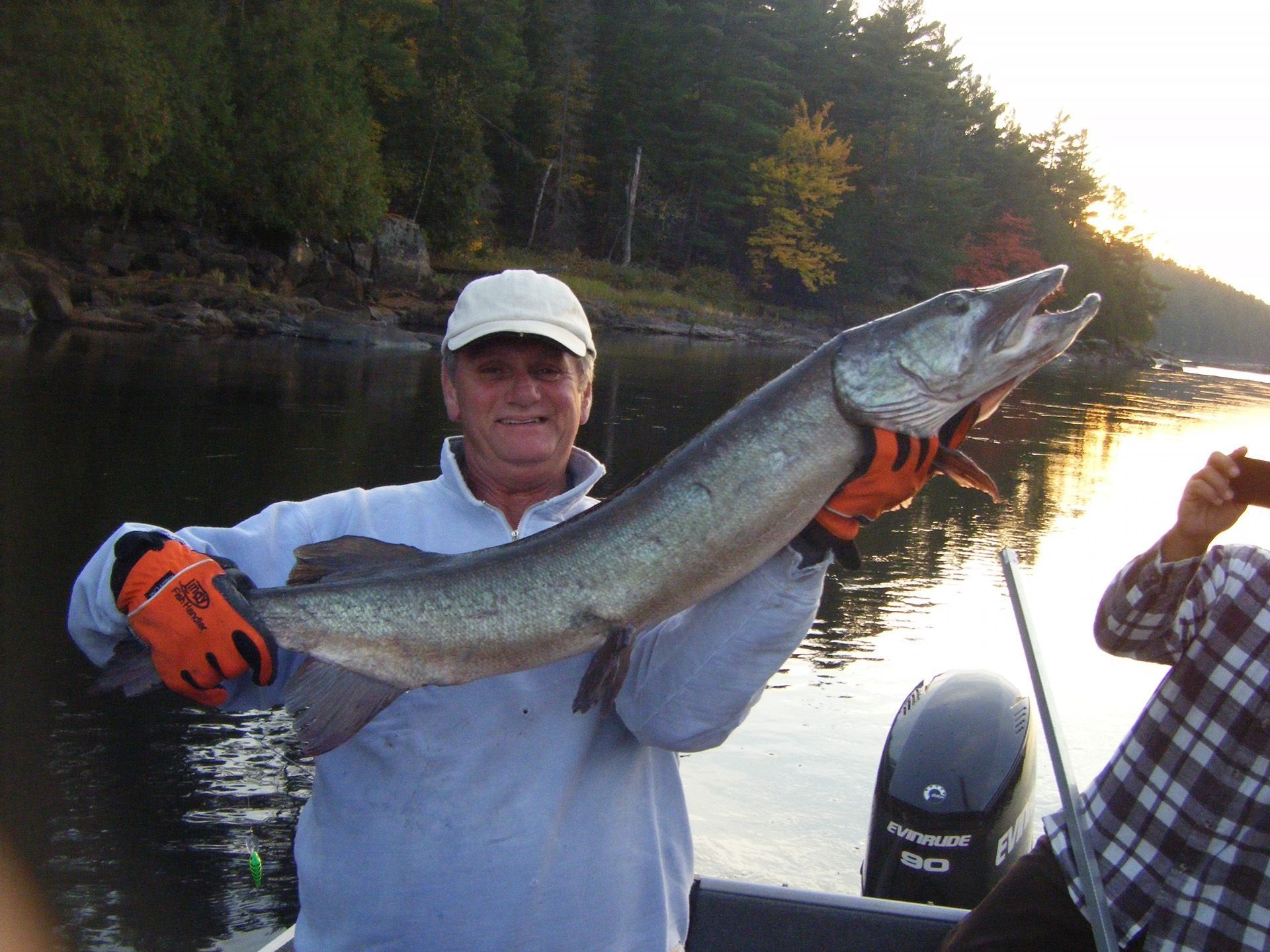 Man holding a long pike while his friend takes a picture of him in the background.