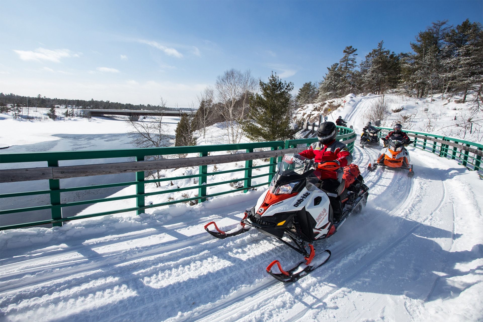 Two snowmobilers cross a snowy bridge along the Gateway to the North tour.