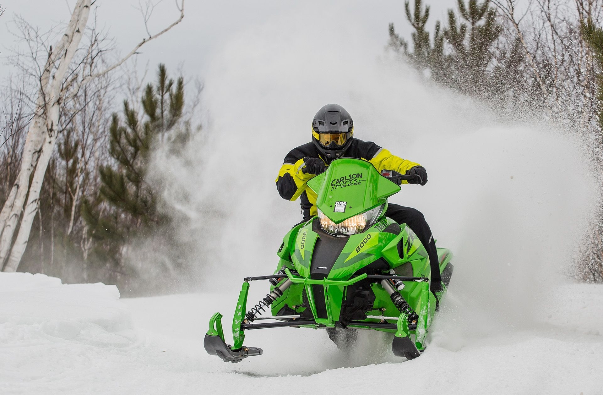 Person riding a green snowmobile kicks up powder.