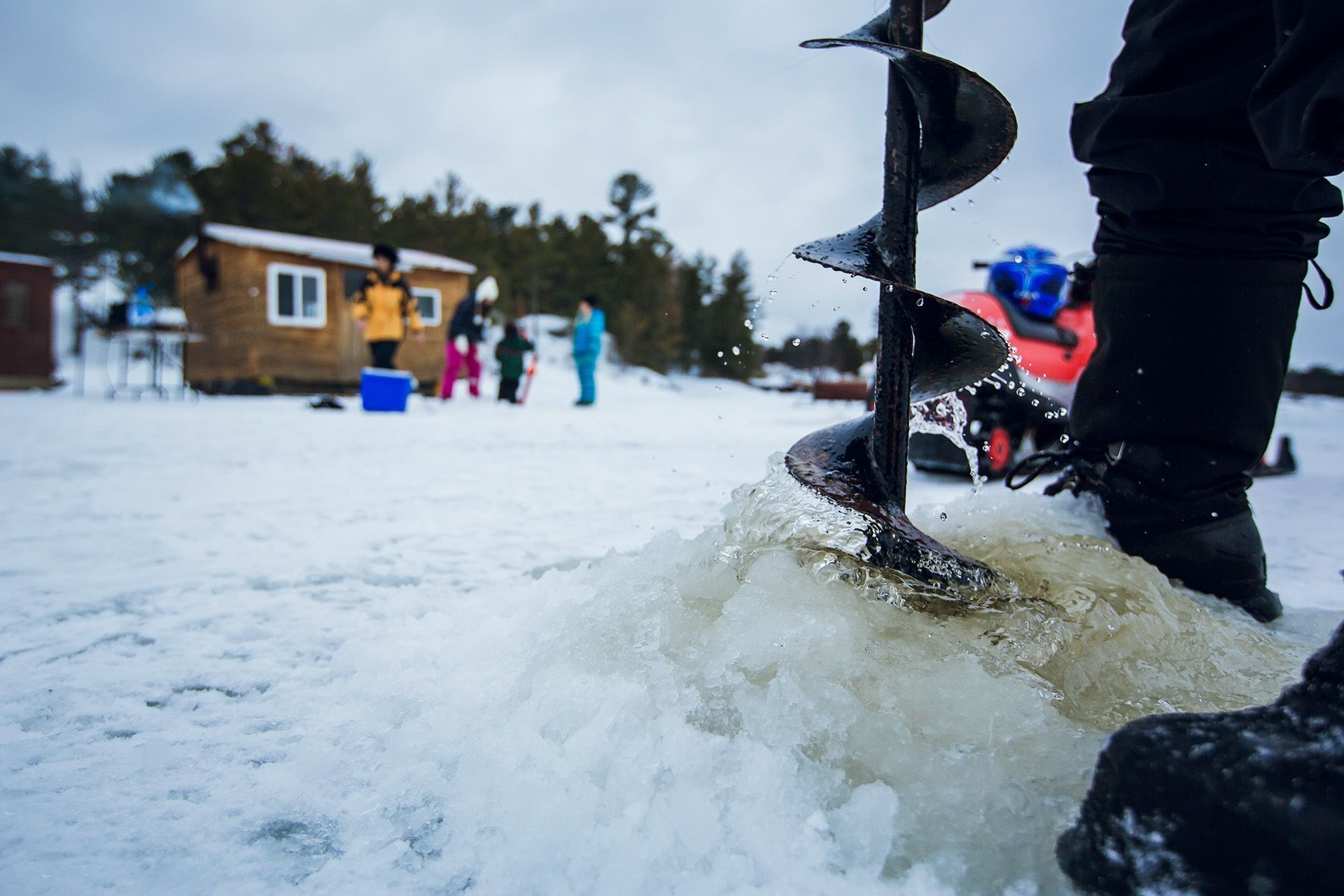 Someone is using an auger to drill a hole for ice fishing near some huts.