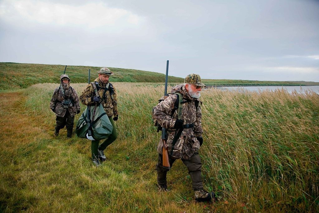 Trois pêcheurs, carabine à l'épaule, marchent près d'un marécage. 