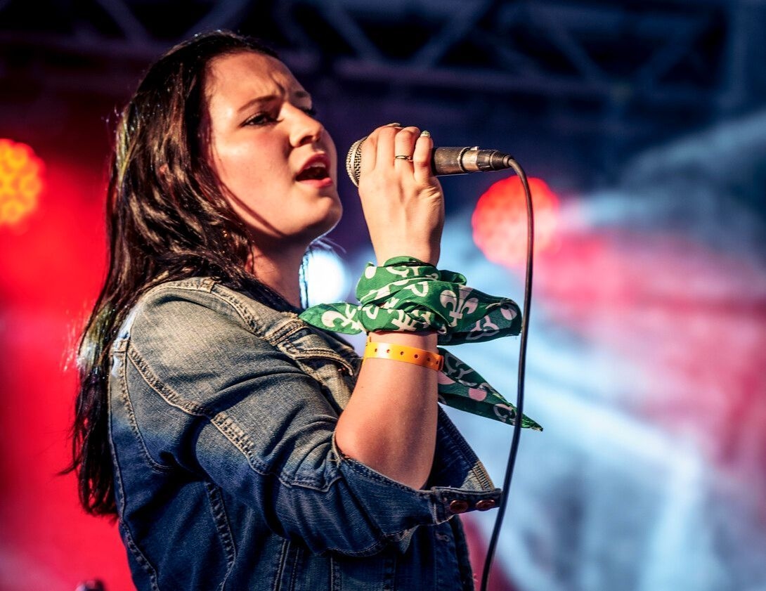 A person singing into a microphone with colourful stage lights behind them.