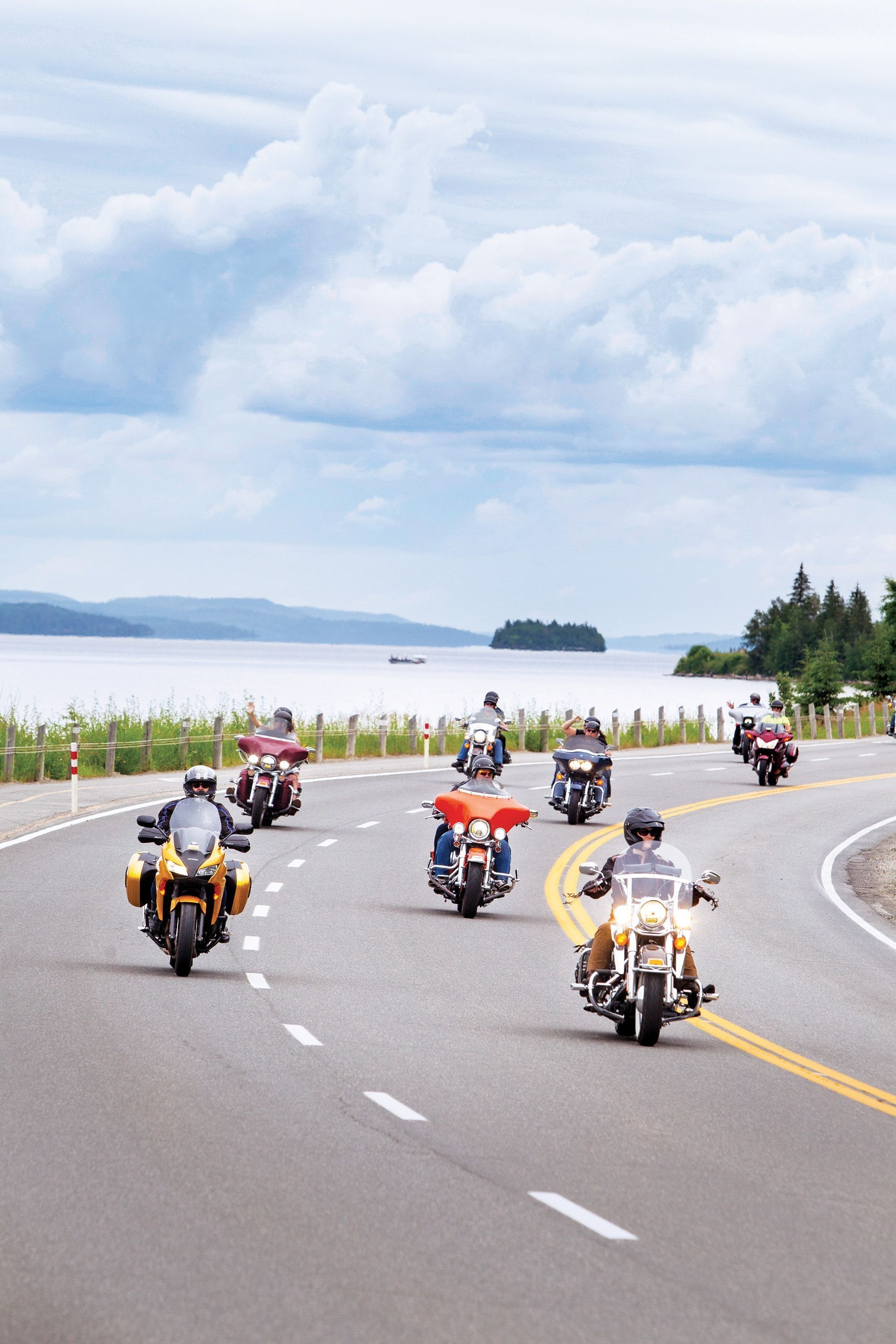 Seven motorcycle drivers take a curving highway road near a lake.