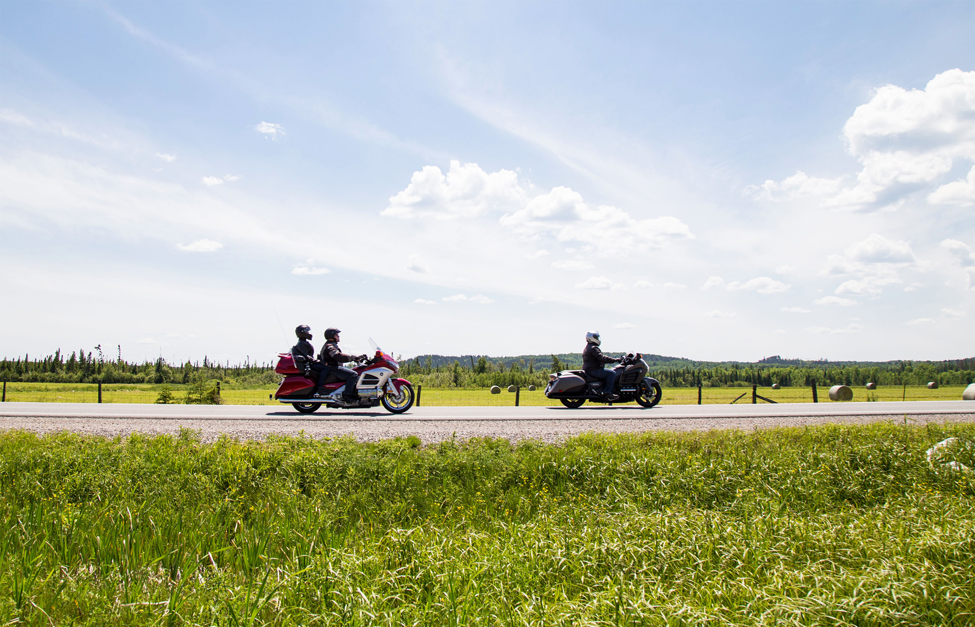 Motorcycles on a stretch of highway next to green fields under the blue sky on a sunny day