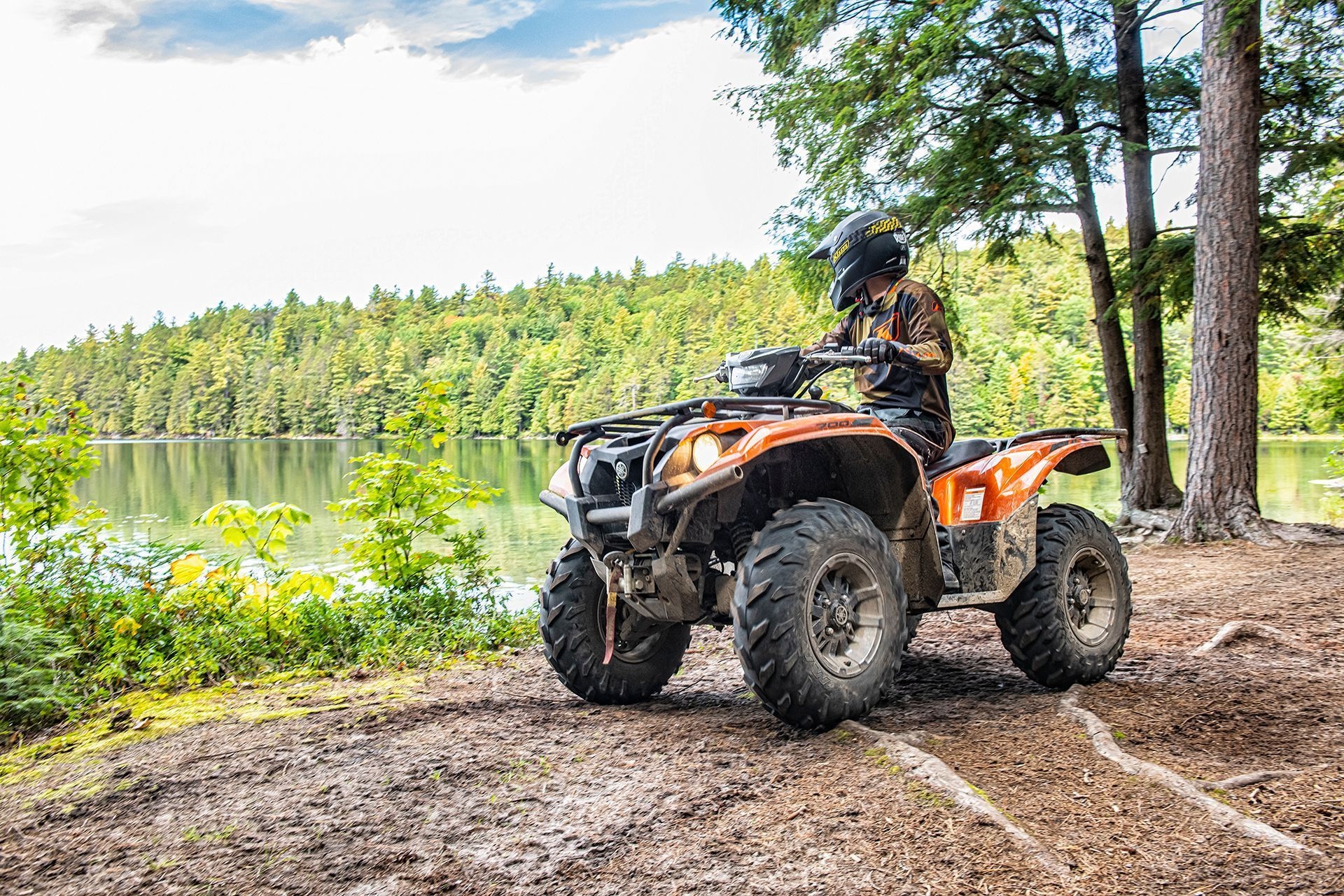 A person on an ATV looks out across a lake and a lush forest