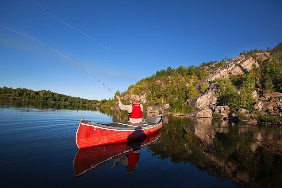 A person in a red canoe sending out their fly fishing line in a swoop overhead.