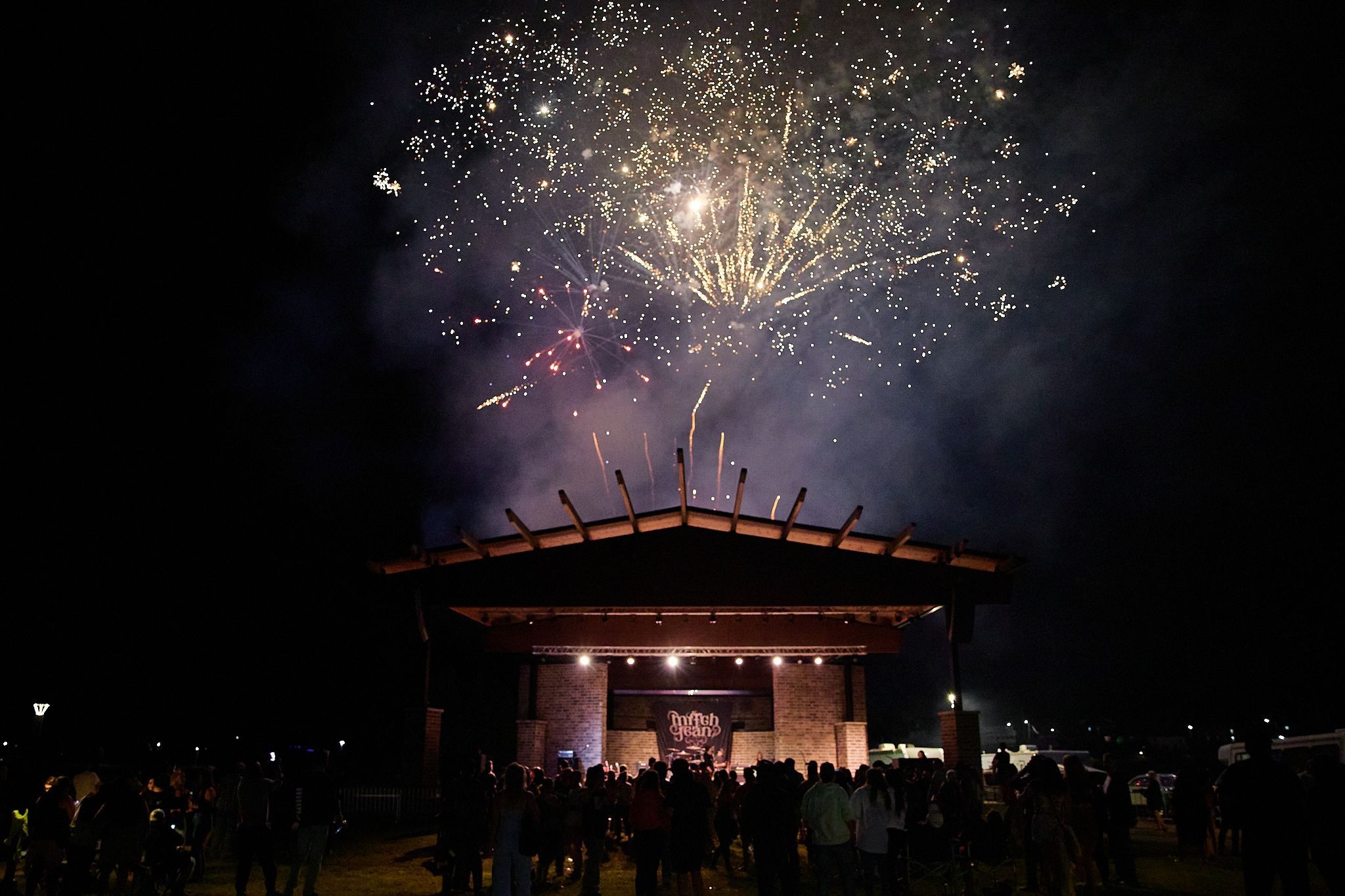 fireworks exploding over an outdoor stage with bright lights and musicians performing