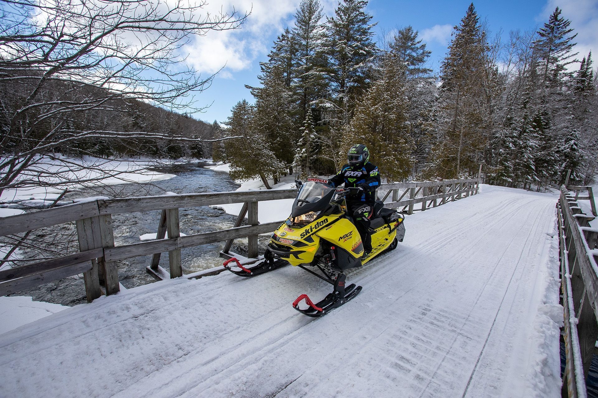 A person on a yellow snowmobile is going across a bridge.