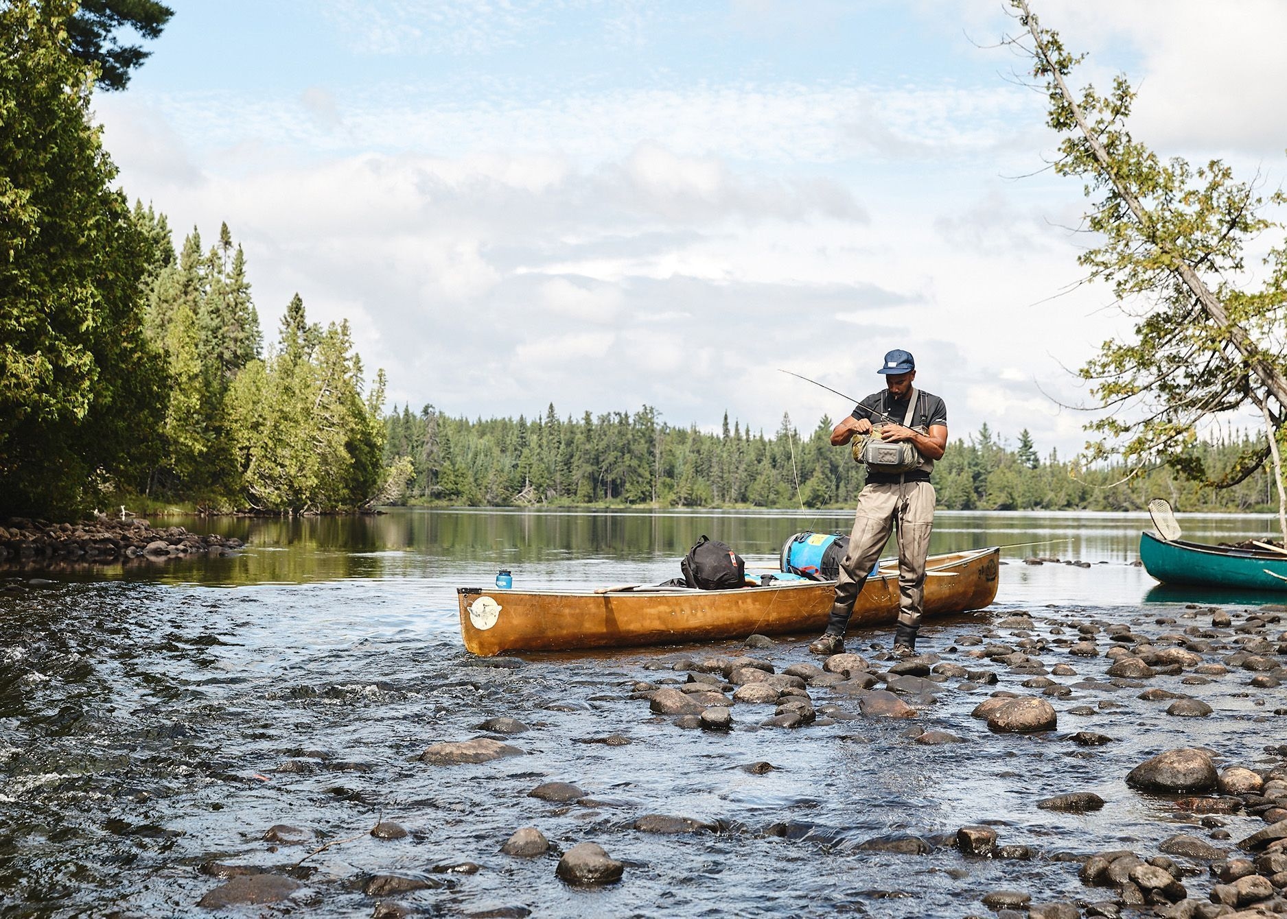 A man is standing in a river fly fishing next to his canoe.