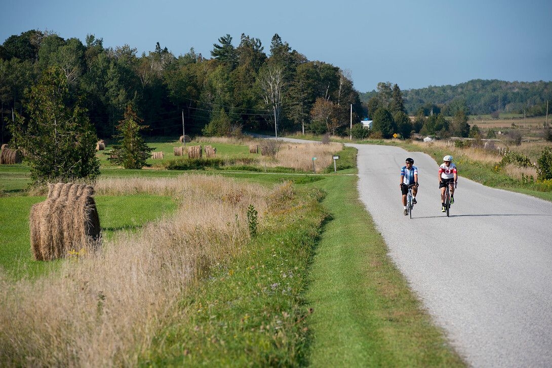 two cyclists ride along a flat stretch of road beside fields and grass