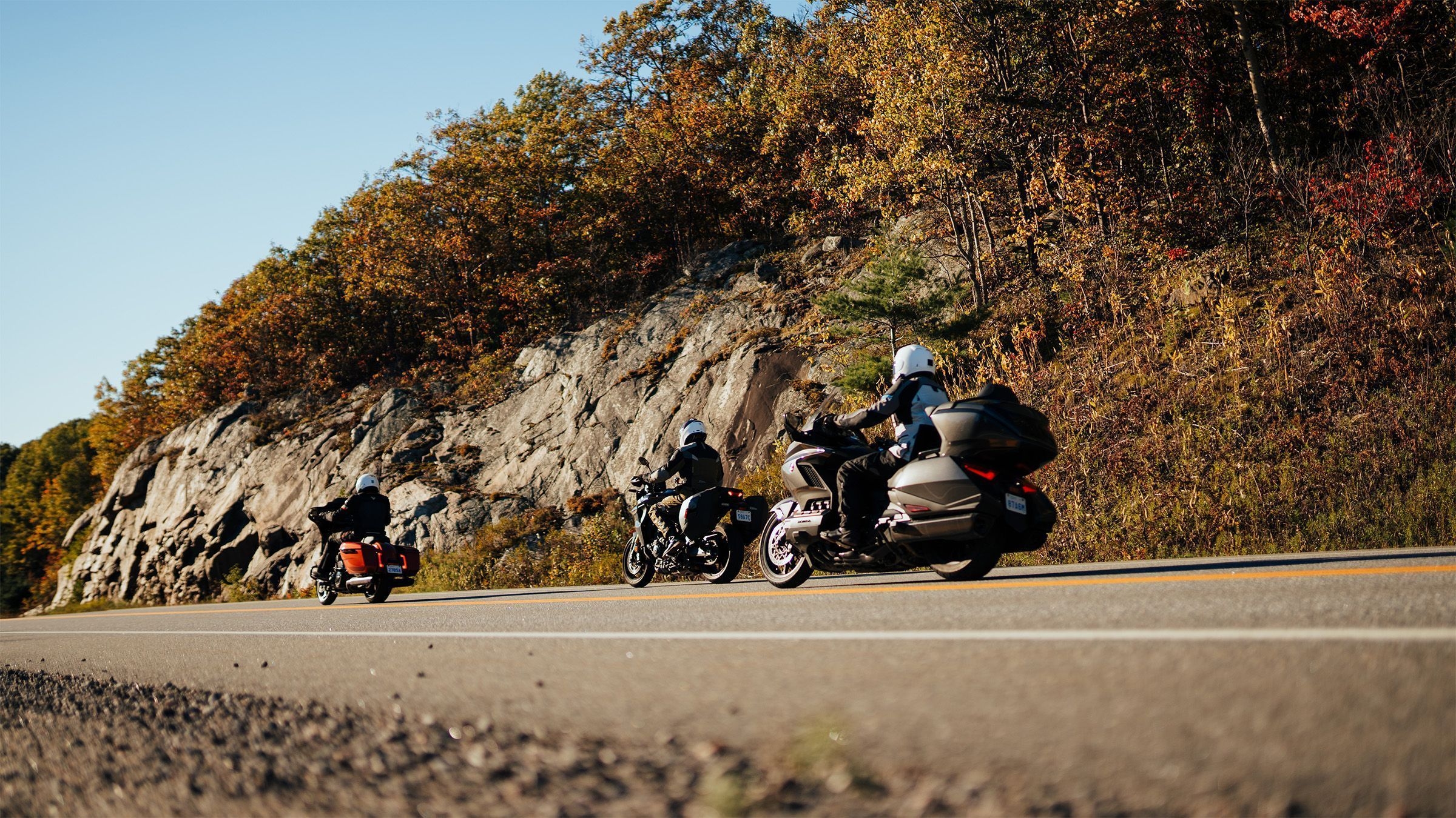 Three motorcycles drive by on a fall day.