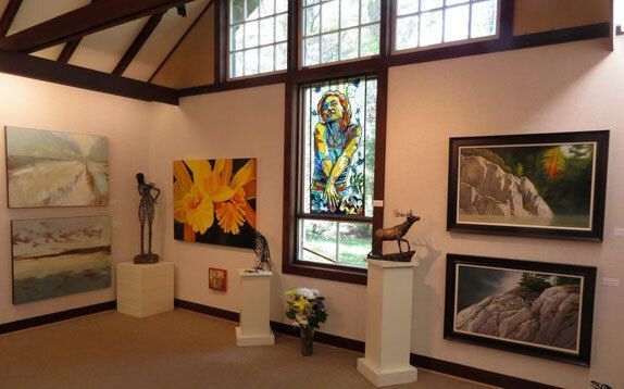 a small white interior of a building showing statues and several framed paintings