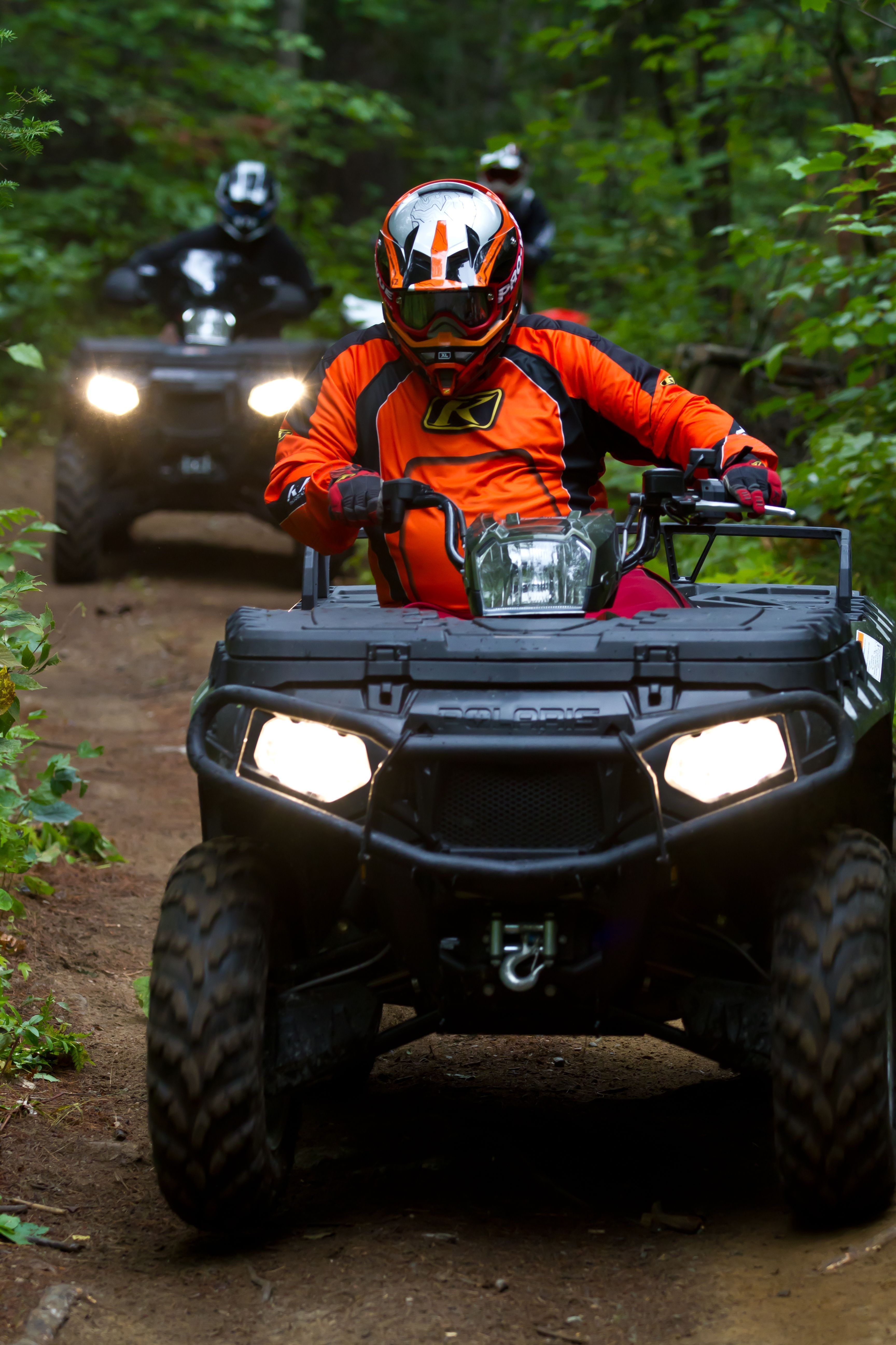 Two people riding ATVs turn a tight corner on a dirt trail.