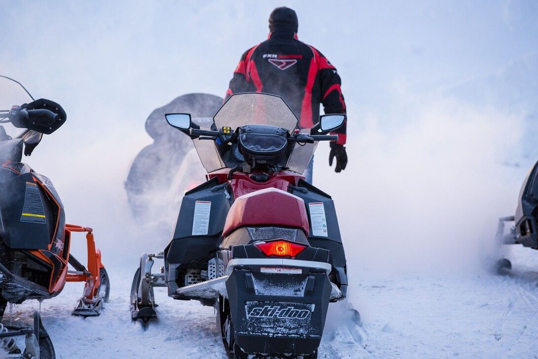 A person stands behind their snowmobile at dusk