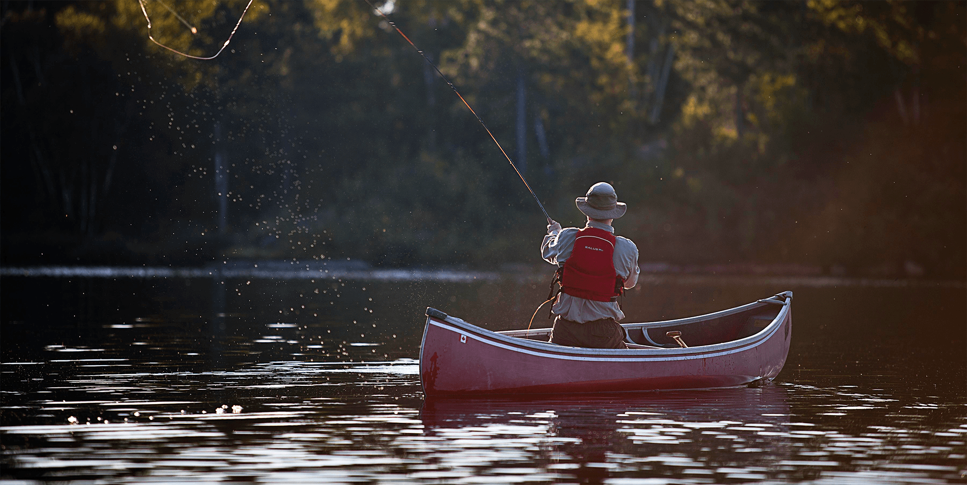 A person casting their line in a red canoe.