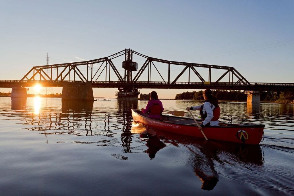 Two people canoeing in front of the Little Current Swing Bridge at sunset.