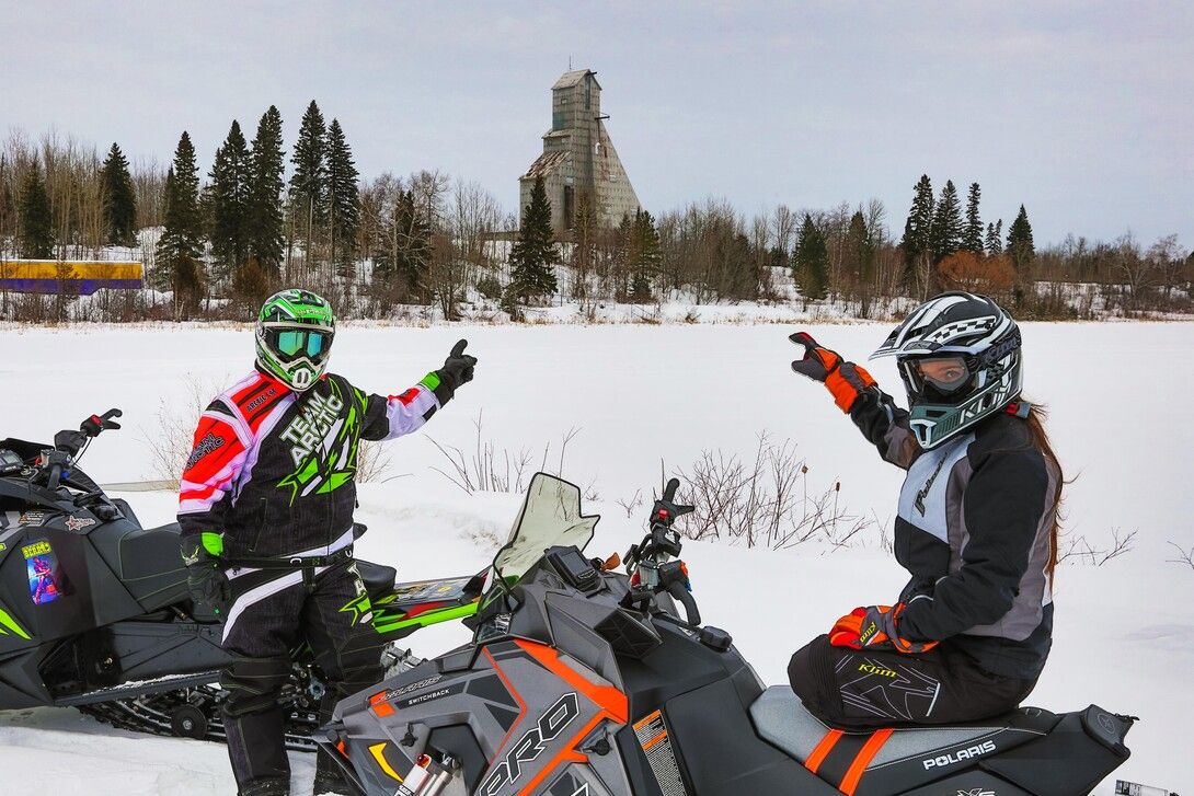 Two people point at the mine in Timmins atop snowmobiles