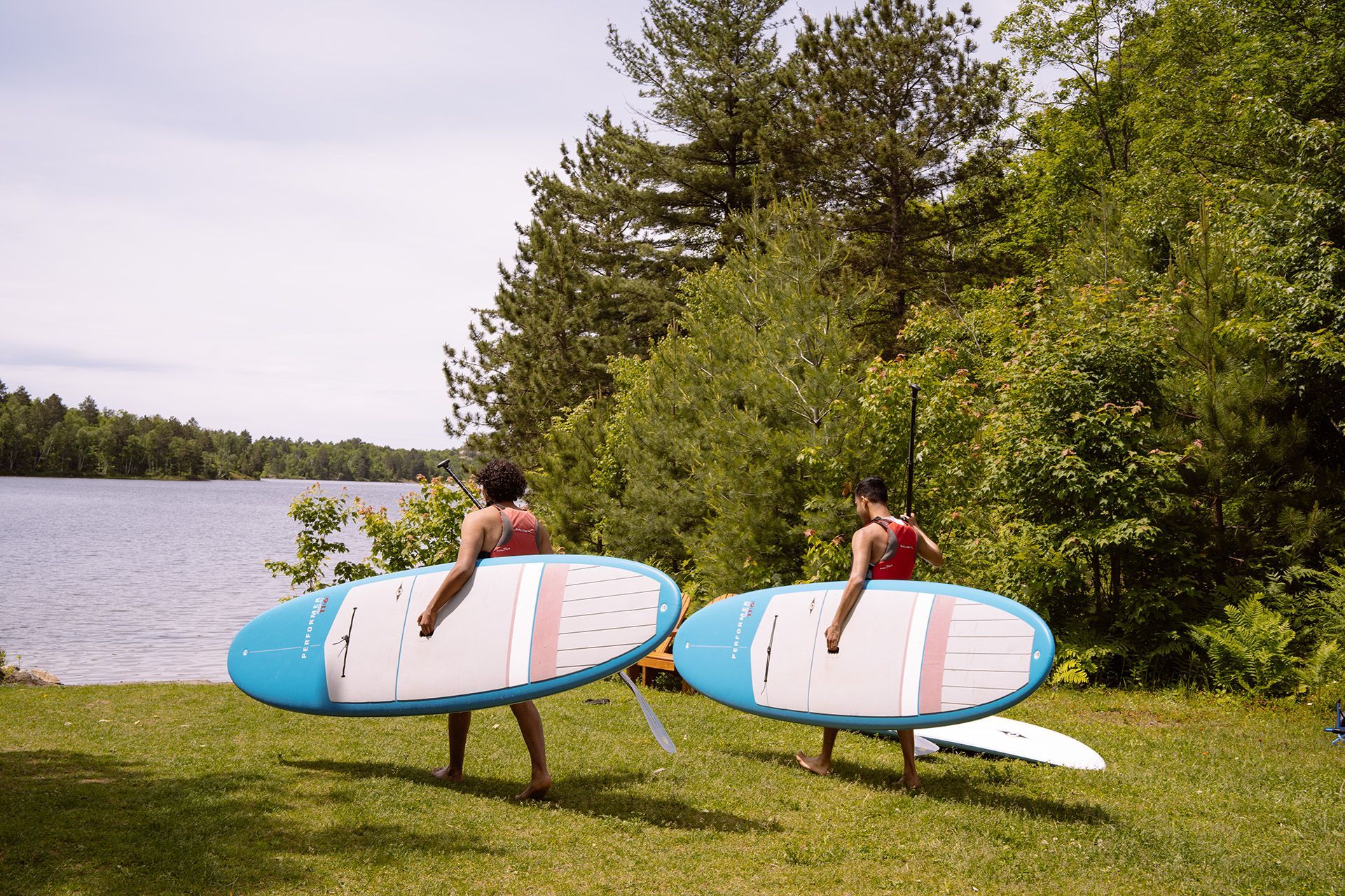 Deux personnes, planche à pagaie sous le bras, se dirigent vers un lac.